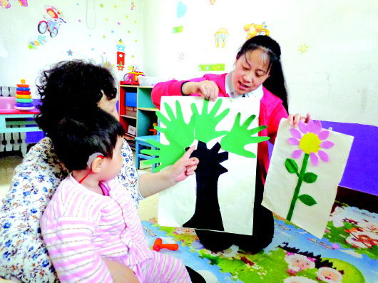 济南瑞峰听觉言语康复中心的特教老师毛阿云(右一)在教孩子识别“花”和“树”。